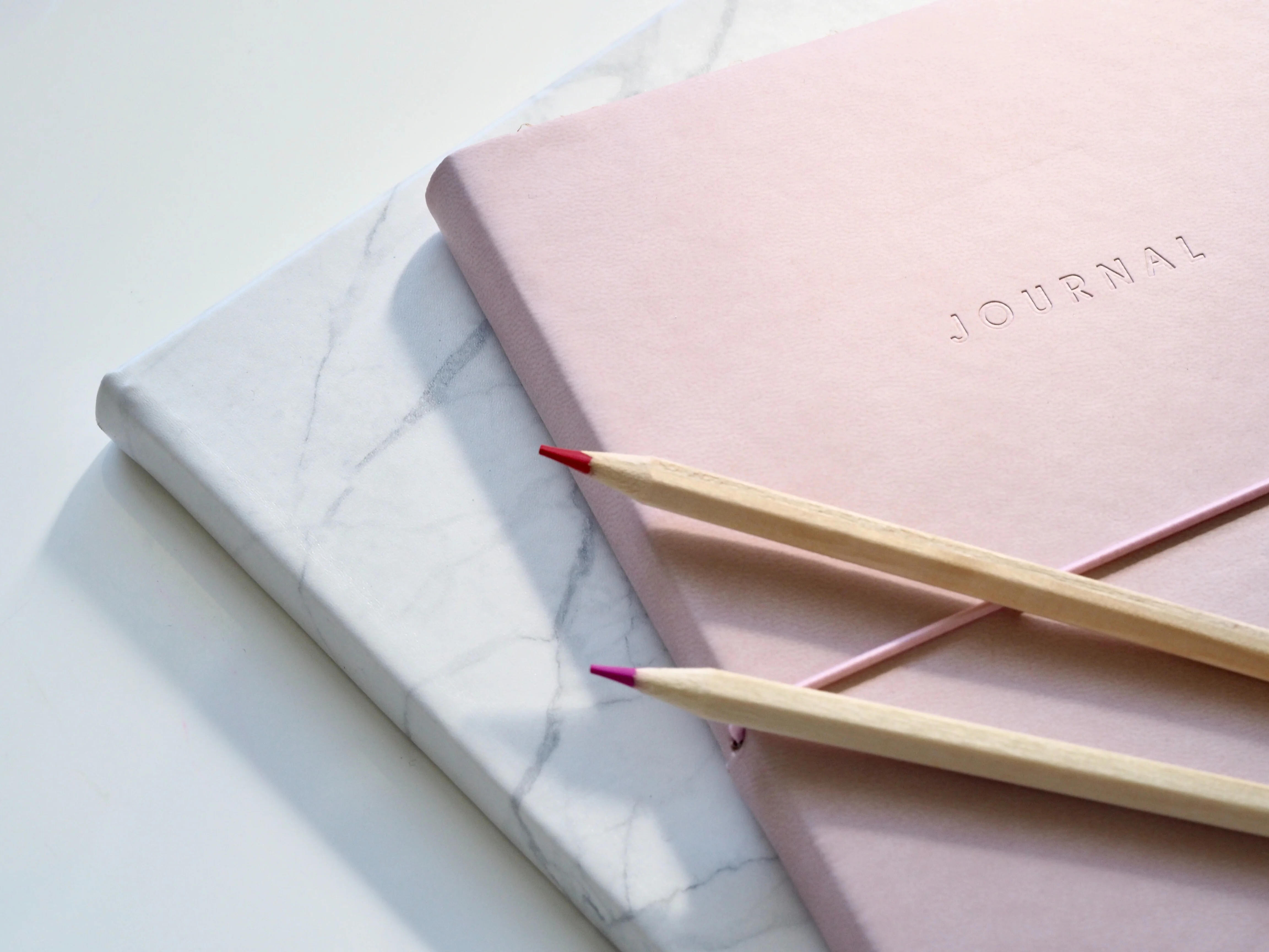 Two color pencils resting on a notebook which has &lsquo;Journal&rsquo; engraved on it.